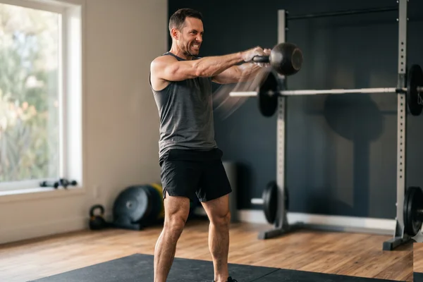 Athletic man in his late thirties at the top of an explosive kettlebell swing, illustrating power training under the new ACSM strength guidelines